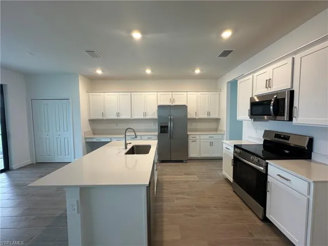 Kitchen with sink, white cabinetry, an island with sink, and stainless steel appliances