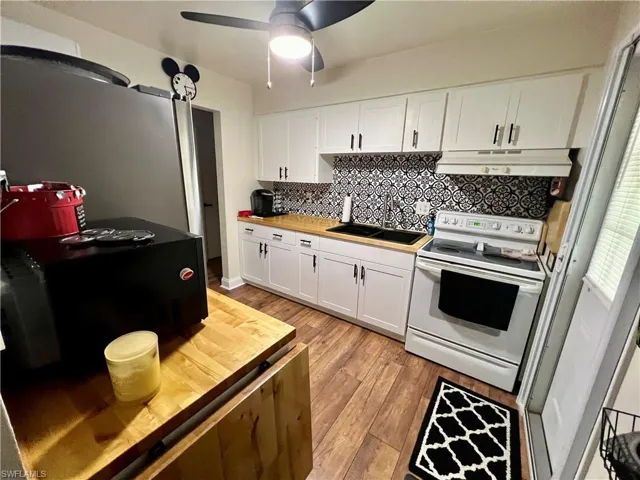 Kitchen with white cabinetry, butcher block countertops, luxury vinyl plank flooring, sink, and electric range