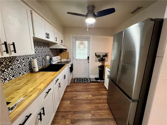 Kitchen featuring white cabinets, stainless steel refrigerator, white electric range, and butcher block counters