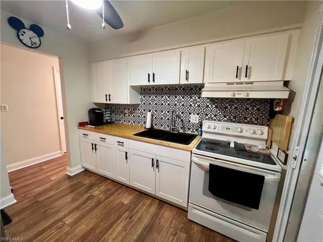 Kitchen with luxury vinyl plank flooring, sink, white cabinets, range with electric cooktop, and butcher block countertops