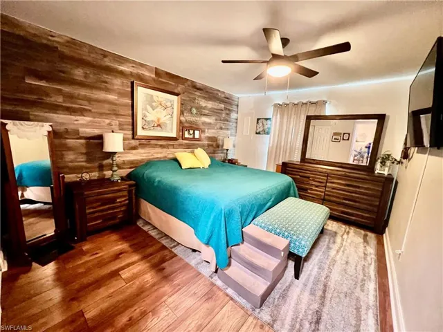 Primary bedroom with luxury vinyl plank flooring, wood accent wall, and ceiling fan