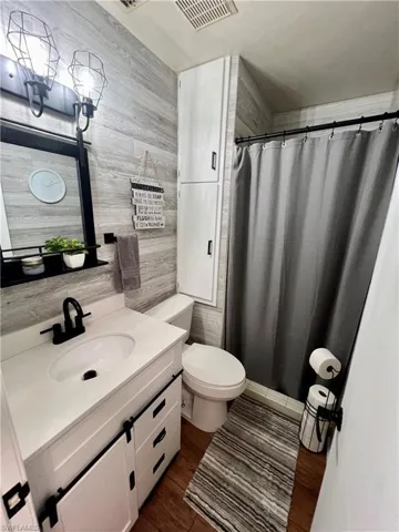 Bathroom featuring light grey luxury vinyl wood like walls, vanity, toilet, and a shower.