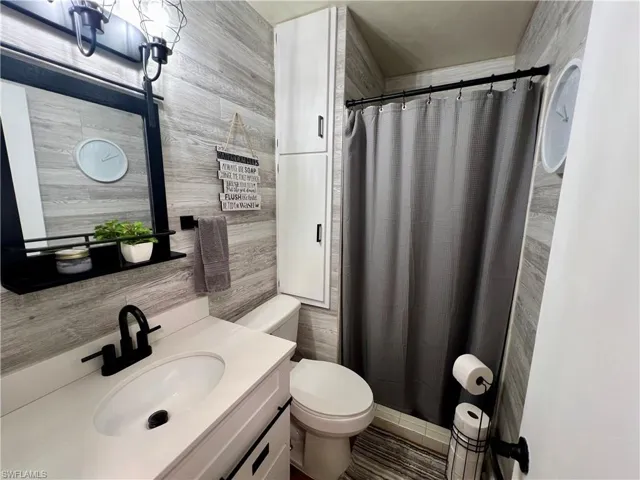 Bathroom featuring light grey luxury vinyl wood like walls, vanity, toilet, and a shower.