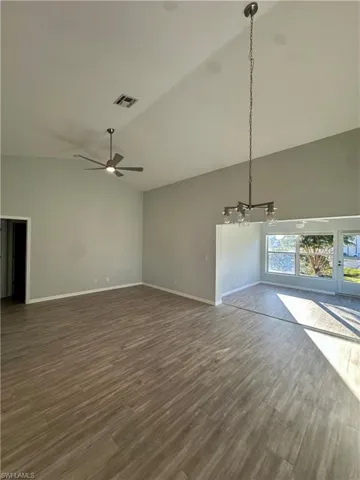 Unfurnished living room with vaulted ceiling, dark wood-type flooring, ceiling fan, and hanging lights