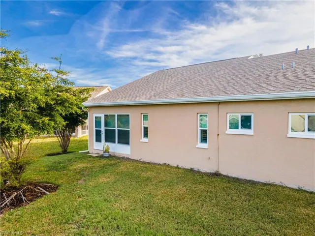 Back of house with a lawn, stucco siding, and a shingled roof