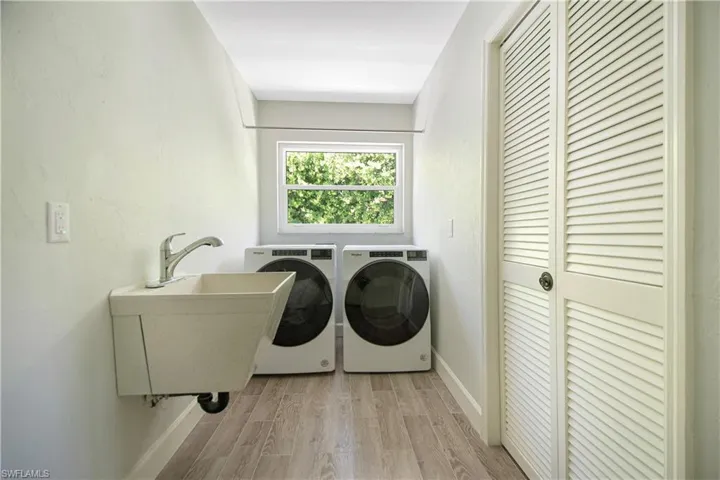 Clothes washing area with separate washer and dryer, sink, and light hardwood / wood-style flooring