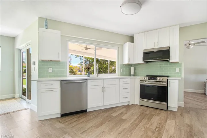 Kitchen featuring light wood-type flooring, stainless steel appliances, white cabinets, tasteful backsplash, and ceiling fan