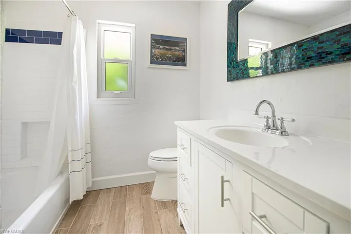 Full bathroom with wood-type flooring, shower / bath combination with curtain, vanity, and toilet