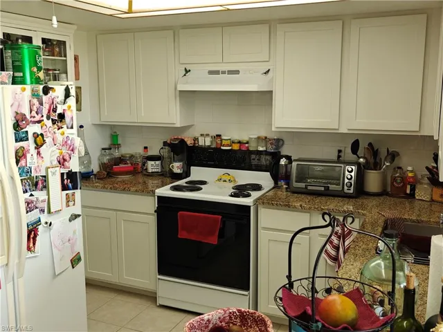 Kitchen featuring light tile patterned floors, dark stone countertops, range with electric cooktop, white refrigerator with ice dispenser, and decorative backsplash