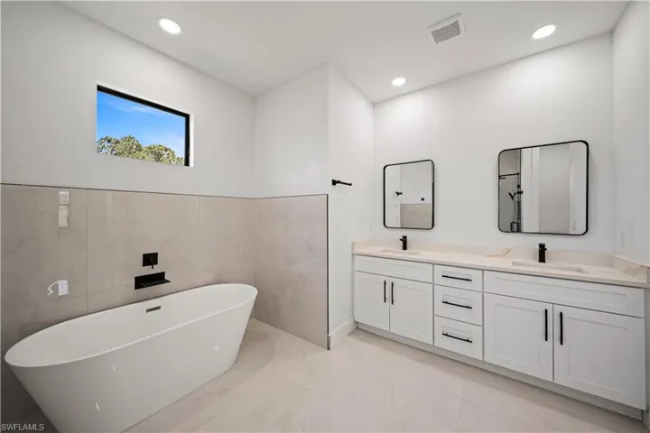 Full bath featuring marble finish floors, double vanity, a freestanding tub, recessed lighting, and tile walls