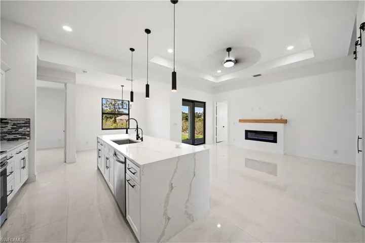 Kitchen featuring a sink, dishwasher, a raised ceiling, a ceiling fan, and light marble finish flooring