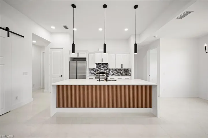 Kitchen featuring stainless steel fridge, a barn door, a sink, white cabinets, and a large island
