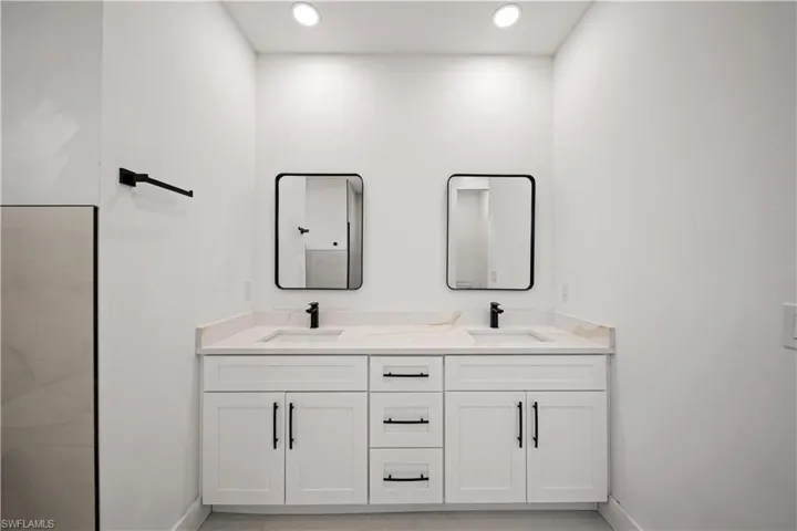 Bathroom featuring double vanity, baseboards, and recessed lighting