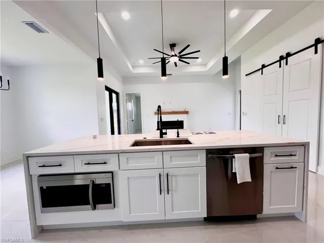 Kitchen with dishwasher, a sink, stainless steel microwave, a raised ceiling, and recessed lighting