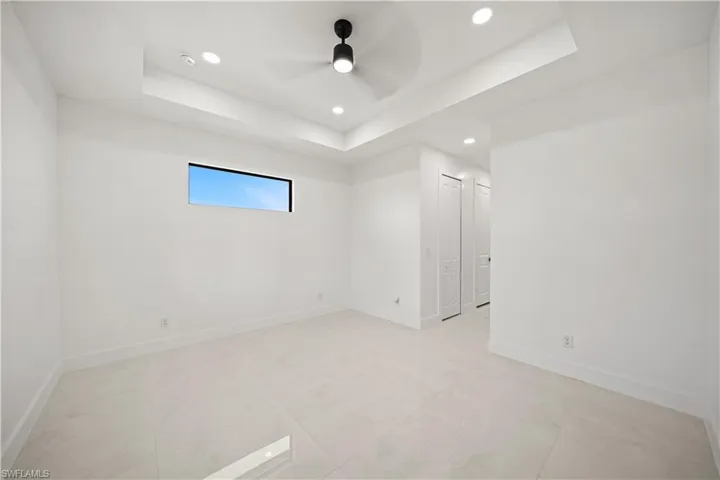 Empty room with recessed lighting, light marble finish flooring, a raised ceiling, and baseboards