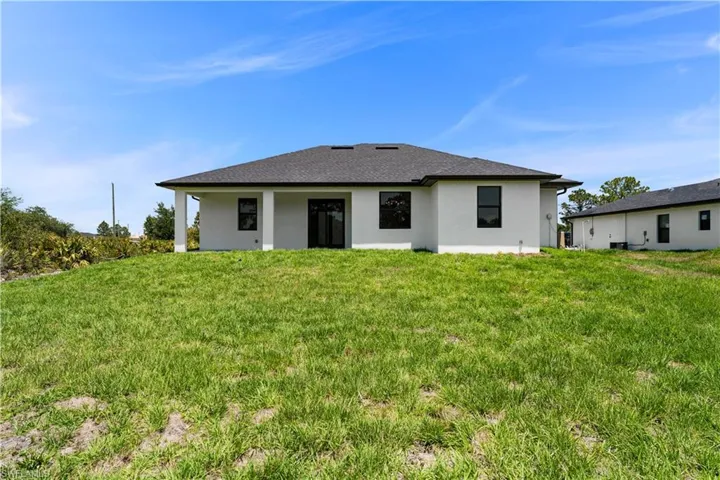 Back of property featuring stucco siding, a yard, and a shingled roof