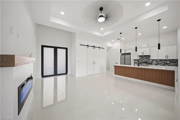 Kitchen featuring stainless steel built in fridge, a barn door, light marble finish floors, ceiling fan, and a large island with sink