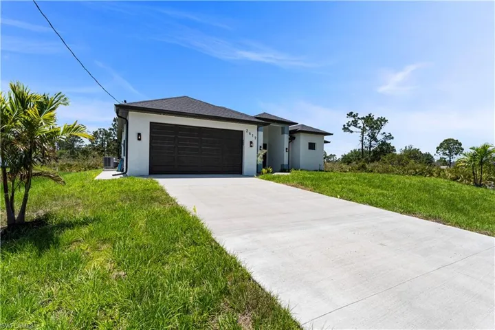 View of front of home with stucco siding, central air condition unit, driveway, and an attached garage