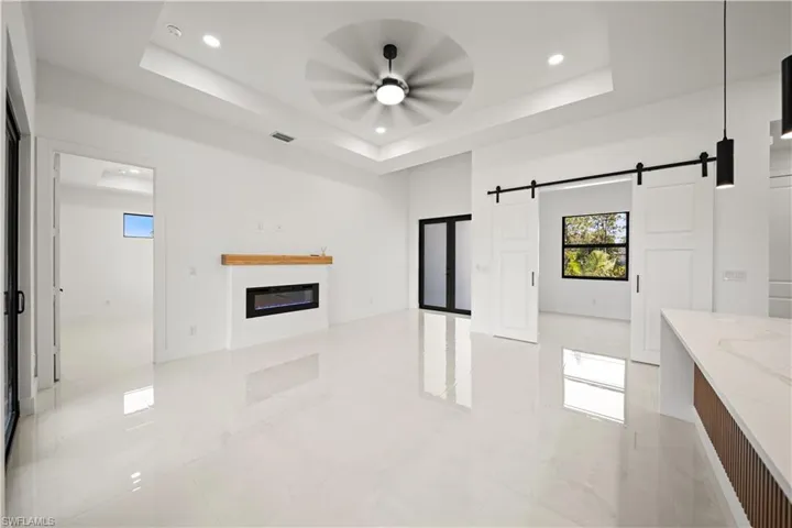 Unfurnished living room featuring a barn door, ceiling fan, a glass covered fireplace, recessed lighting, and a raised ceiling