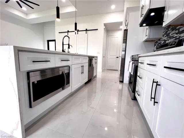Kitchen with appliances with stainless steel finishes, light marble finish flooring, a barn door, recessed lighting, and white cabinetry