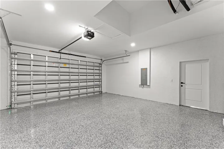Garage featuring electric panel, a textured wall, a garage door opener, and recessed lighting