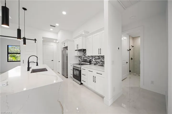 Kitchen featuring a sink, appliances with stainless steel finishes, light marble finish floors, a barn door, and white cabinetry