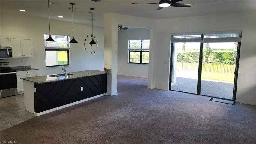 Open-concept living space featuring a kitchen island with pendant lighting, white cabinetry, granite countertops, and stainless steel appliances
