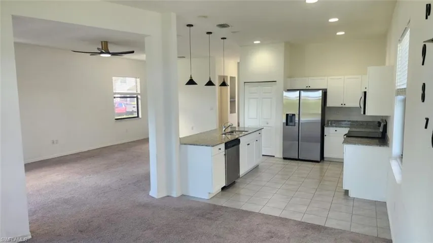 Open-concept kitchen and living area featuring white cabinetry, granite countertops, stainless steel appliances, and a central island with sink