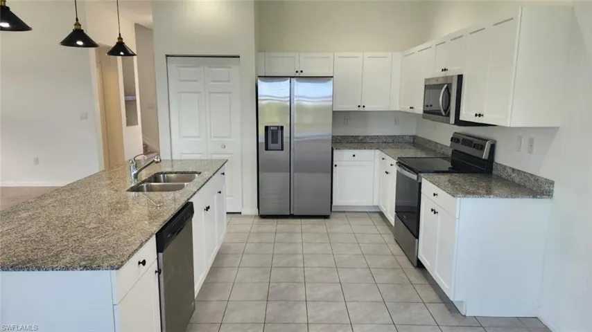 Kitchen featuring white cabinetry, light-toned stone countertops, stainless steel appliances, and tile flooring