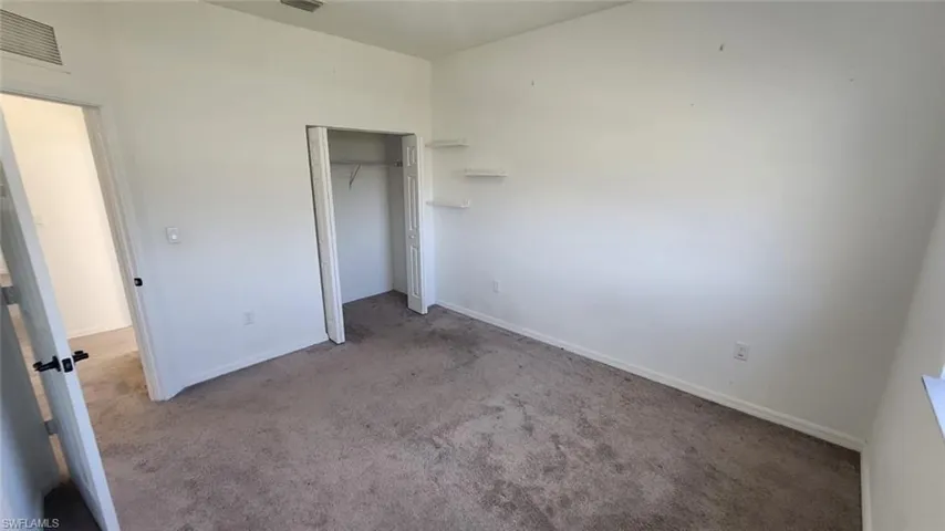 Carpeted room with white walls, a built-in closet, and wall-mounted shelving