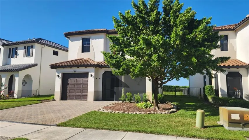 Mediterranean-style residence featuring a tile roof, stucco exterior, patterned paver driveway, attached garage with a panel door, and manicured front landscaping