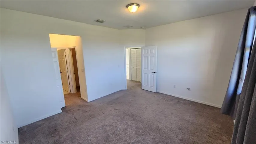 Spacious room featuring neutral carpeting, light-toned walls, and a ceiling-mounted light fixture