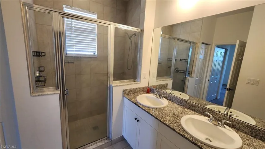 Bathroom featuring a glass-enclosed shower with tile surround, a dual vanity with undermount sinks, stone countertops, and a full-width mirror