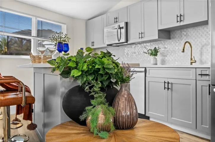 Kitchen featuring stainless steel microwave, decorative backsplash, dishwasher, and light stone counters