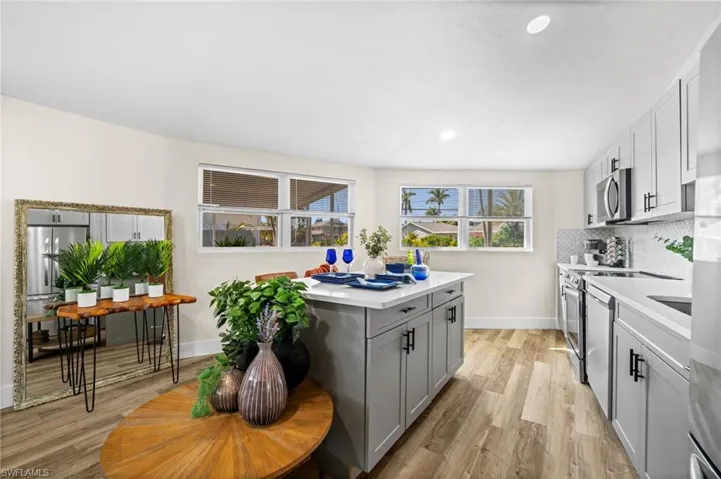 Kitchen with light wood-style floors, gray cabinetry, stainless steel appliances, backsplash, and light stone countertops