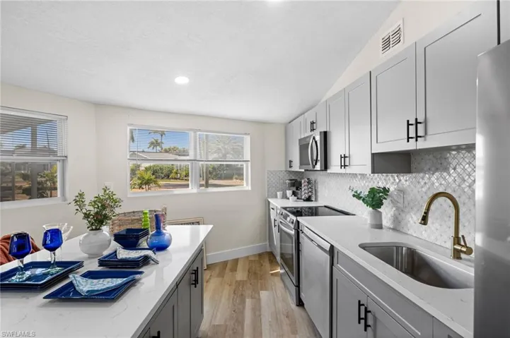 Kitchen featuring gray cabinets, light stone counters, stainless steel appliances, light wood-style floors, and decorative backsplash