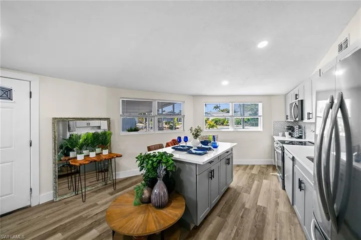 Kitchen with gray cabinetry, stainless steel appliances, light wood-type flooring, light stone counters, and a center island