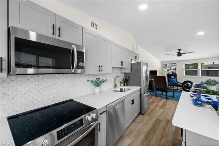 Kitchen featuring stainless steel appliances, a ceiling fan, light stone countertops, gray cabinets, and light wood-type flooring