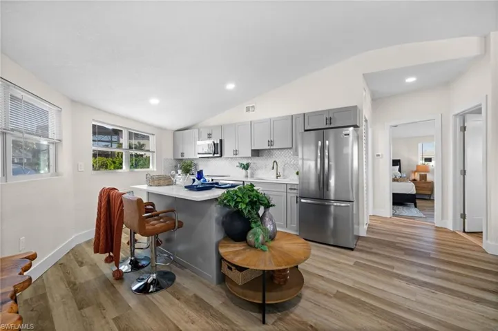 Kitchen featuring gray cabinets, lofted ceiling, stainless steel appliances, a kitchen bar, and light wood-style floors