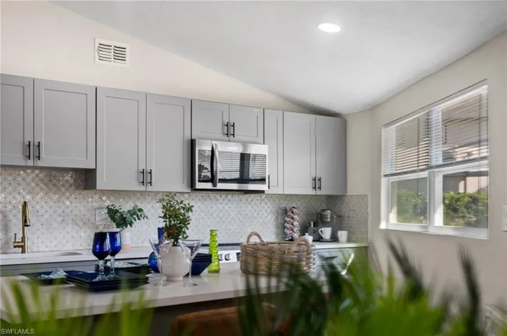 Kitchen with gray cabinetry, lofted ceiling, stainless steel microwave, and tasteful backsplash