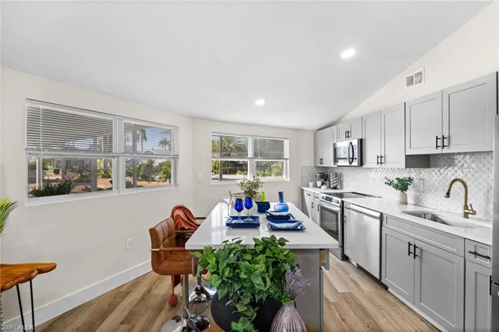 Kitchen featuring gray cabinets, light wood-type flooring, decorative backsplash, stainless steel appliances, and vaulted ceiling