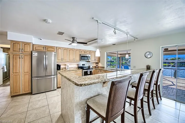 Kitchen featuring decorative light fixtures, light stone counters, kitchen peninsula, track lighting, and appliances with stainless steel finishes