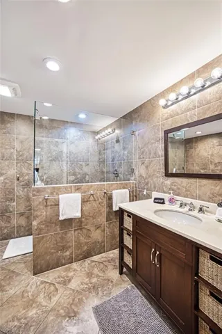 Bathroom featuring tiled shower, tile flooring, vanity, and tile walls