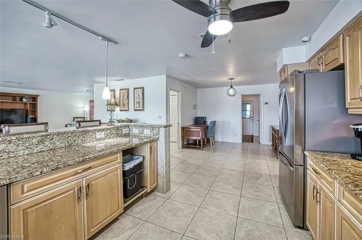 Kitchen with light stone countertops, pendant lighting, track lighting, ceiling fan, and light tile floors