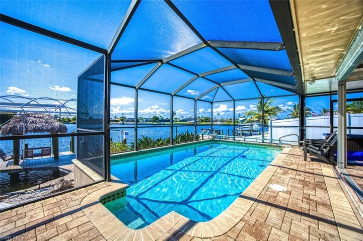 View of pool featuring glass enclosure, a water view, and a patio area