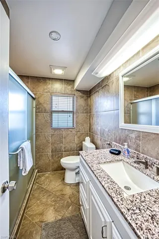 Bathroom with tile floors, vanity, toilet, and tile walls