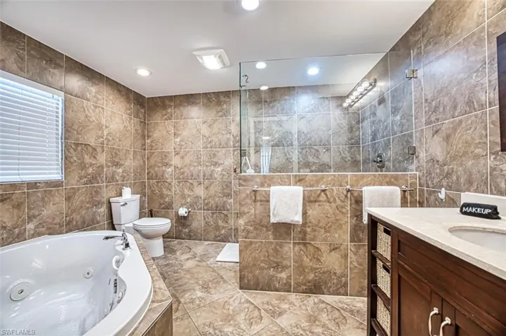 Full bathroom with tile flooring, tile walls, toilet, and vanity