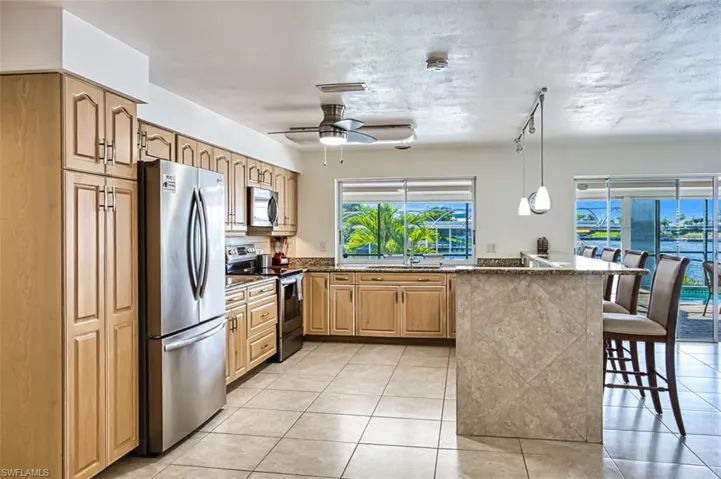 Kitchen featuring stainless steel appliances, ceiling fan, a breakfast bar area, light tile floors, and pendant lighting