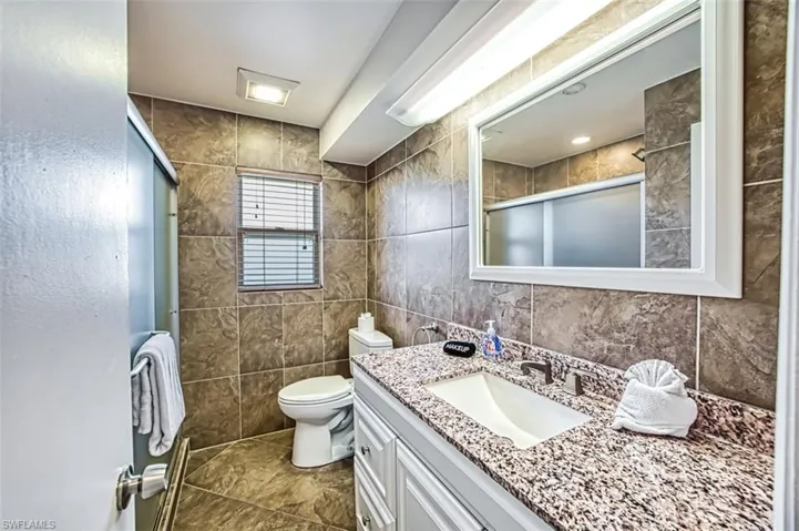 Bathroom with tile floors, vanity with extensive cabinet space, toilet, and tile walls