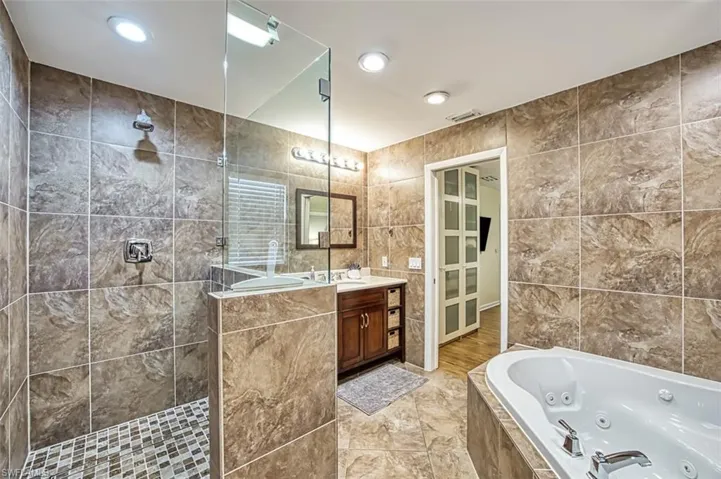 Bathroom with plus walk in shower, tile flooring, vanity with extensive cabinet space, and tile walls